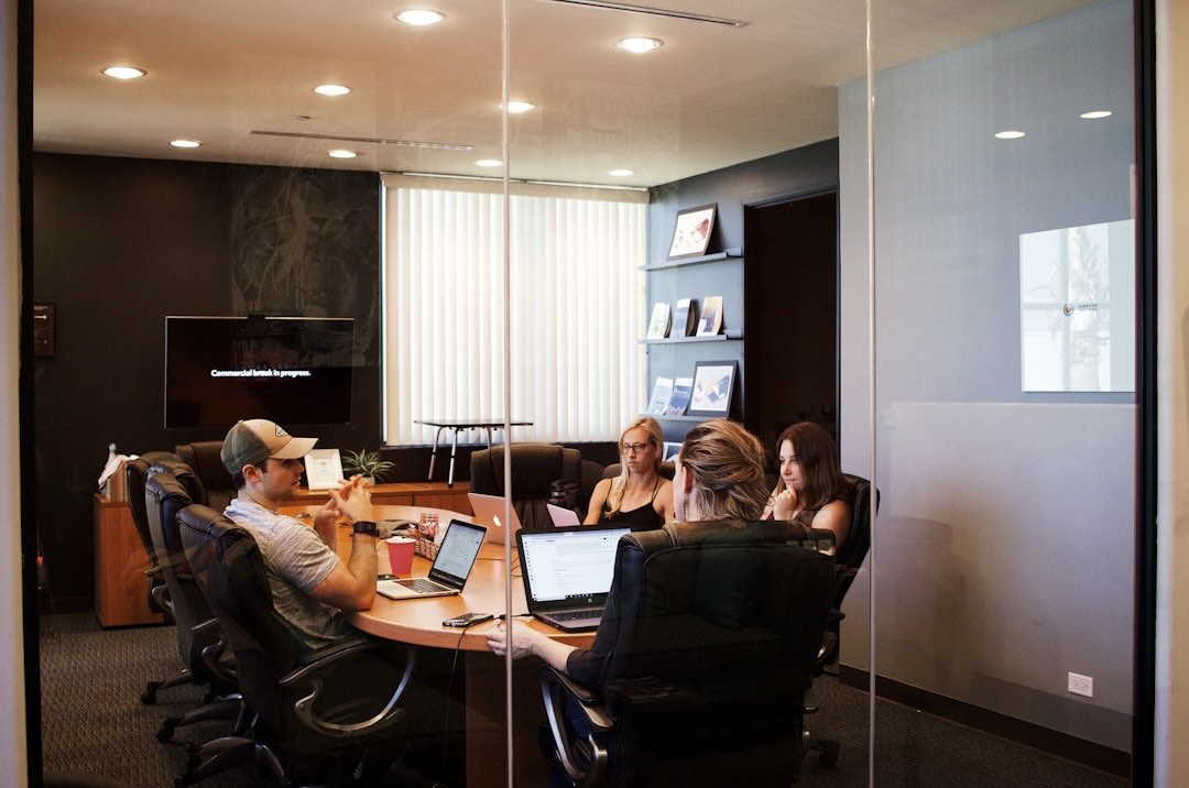 People engaged in knowledge management gather around a table, utilizing laptops to exchange ideas and information.